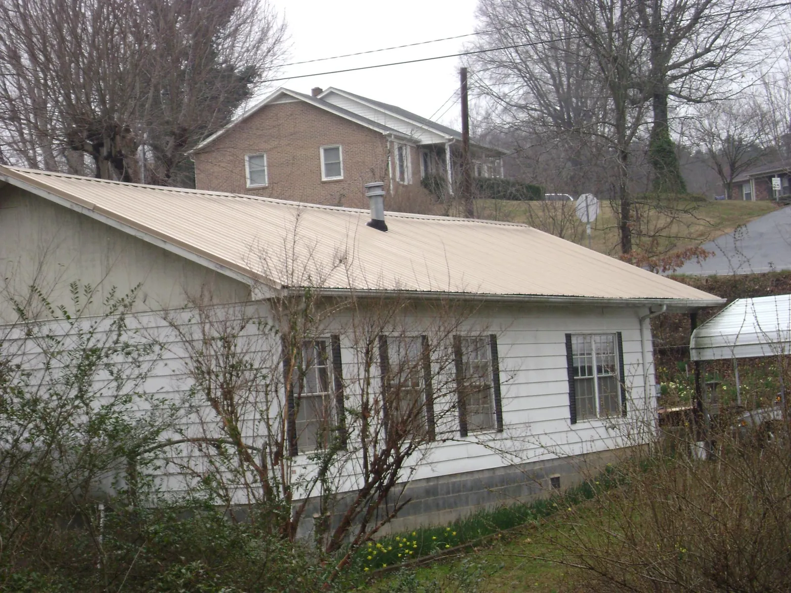 Tan metal roof on a white sided house set into a hillside — Commercial Roofing by Roofing Brothers in Graysville